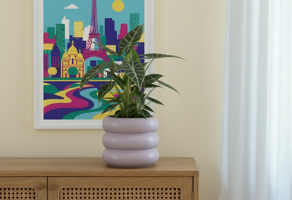 Photo de présentation avec un pot en céramique lila posé sur un meuble en canage devant un mur jaune pâle où il y a accroché un tableau pop de paris. La photo sert à illustrer l'article : Pot ou cache-pot : le guide pour ne plus se tromper