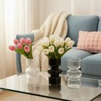 Photo des vases tulipe blanc noir et transparent sur une table en verre devant un canapé bleu.